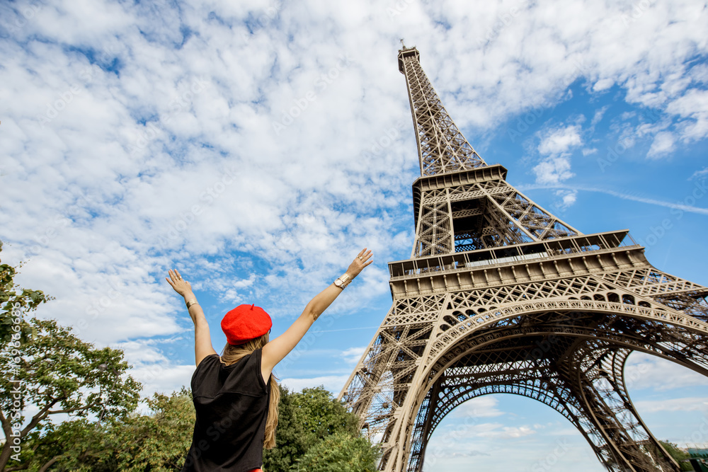 Φωτογραφία Young woman tourist in red cap looking with raised hands on the Eiffel tower in