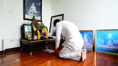 Man kneeling and making prostration to the triple gem at a set of altar table.Buddhist in white dress practicing self discipline by observing the five precepts on buddhist holy day,religion concept.