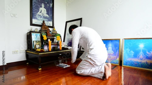 Man kneeling and making prostration to the triple gem at a set of altar table.Buddhist in white dress practicing self discipline by observing the five precepts on buddhist holy day,religion concept. photo