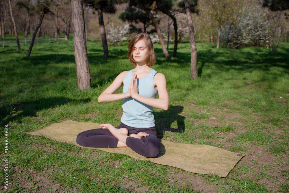 Young fit yoga woman meditating and relaxing in lotus on the green grass, city park background Young fit yoga woman meditating and relaxing in lotus on the green grass, city park background