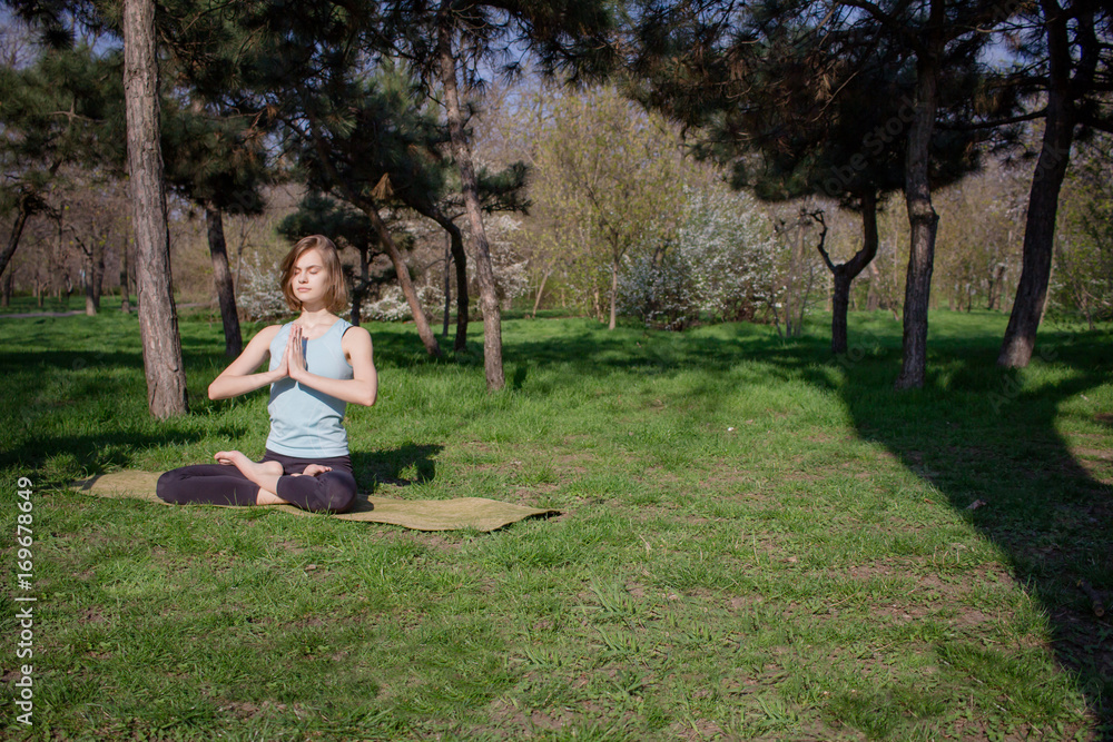 Young fit yoga woman meditating and relaxing in lotus on the green grass, city park background Young fit yoga woman meditating and relaxing in lotus on the green grass, city park background