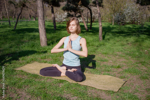 Young fit yoga woman meditating and relaxing in lotus on the green grass, city park background 