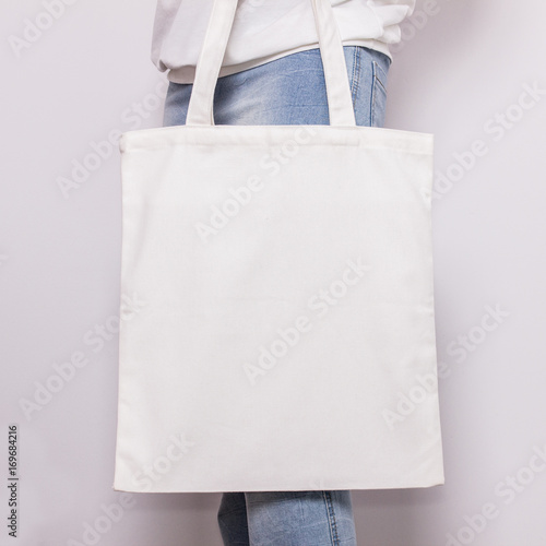 Girl in blue jeans holds blank cotton eco tote bag, design mockup. Handmade shopping bag for girls