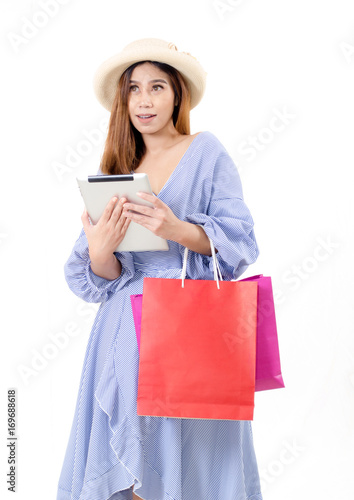 portrait of cheerful asian young woman with hat holding shopping bags looking up and holding tablet in hand isolated on white background, online shopping, lifestyle technology concept, soft focus