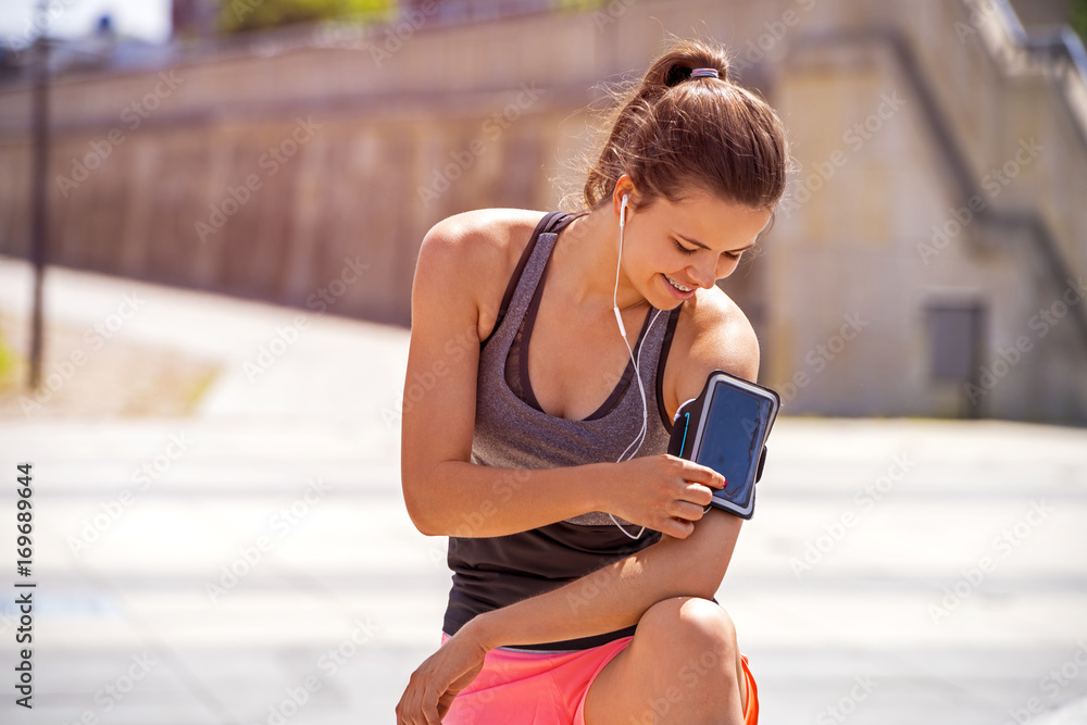 Sporty woman touching phone screen in arm sport band before running. Female athlete listening music while doing sport.