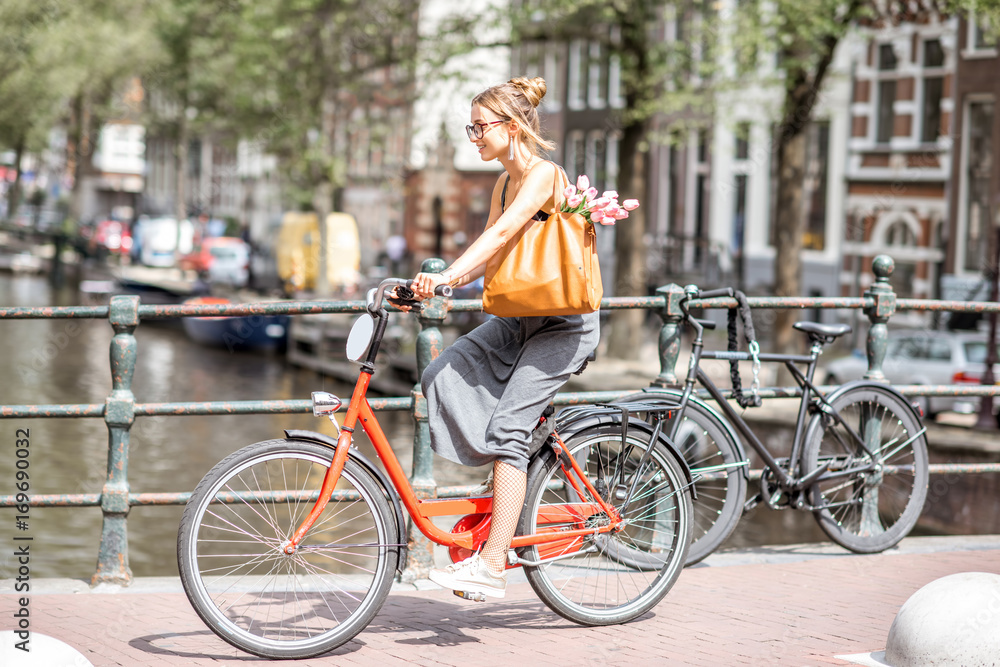 Naklejka premium Młoda piękna kobieta, jazda na rowerze na moście nad kanałem wodnym w starym mieście w Amsterdamie