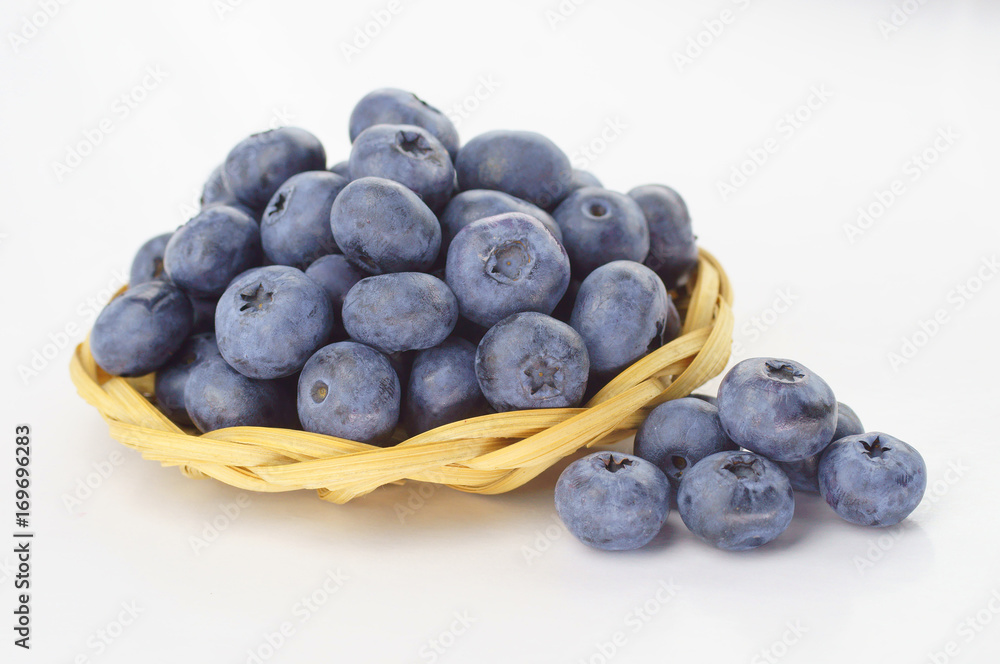Ripe berry blueberries in a straw plate on a white background Ripe berry blueberries in a straw plate on a white background