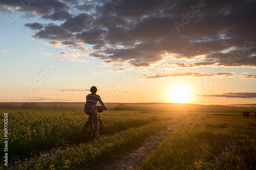 Girl on a bicycle in a field on the road against the sunset background