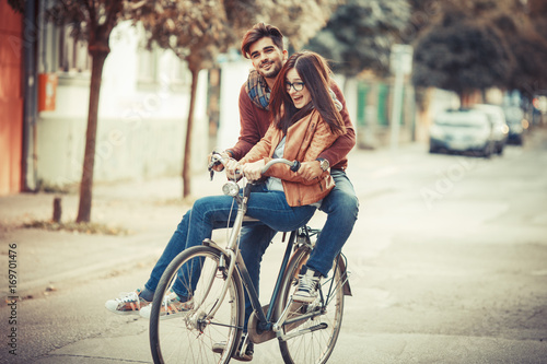 Young couple riding bicycle at the street on autumn day.They sitting on bike and making fun. © BalanceFormCreative