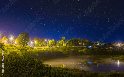Night landscape of the old town with shining streetlight. Night sky with stars. Misty fog on river.