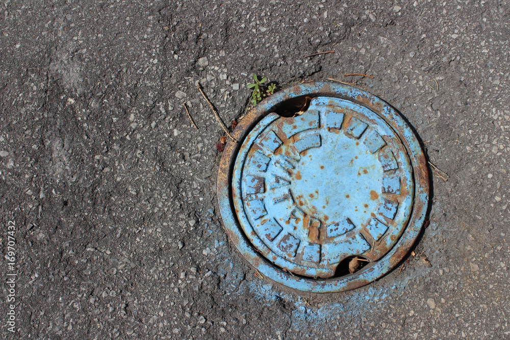 Pipe cover with flaking blue paint, surrounded by asphalt Pipe cover with flaking blue paint, surrounded by asphalt