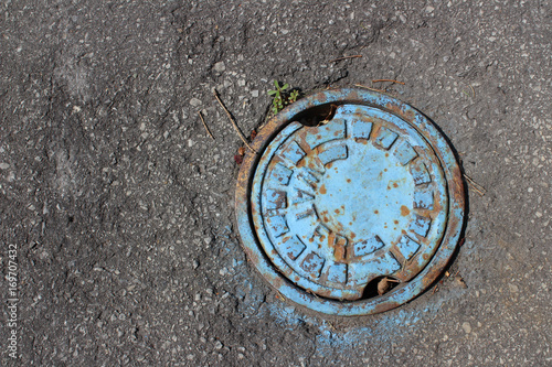 Pipe cover with flaking blue paint, surrounded by asphalt 