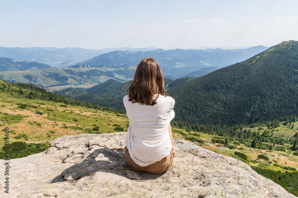 Back of young female person sitting on top of the rock in ukrainian carpathian mountains. Girl tourist enjoys gorgeous landscape scenery on hot sunny day Back of young female person sitting on top of the rock in ukrainian carpathian mountains. Girl tourist enjoys gorgeous landscape scenery on hot sunny day