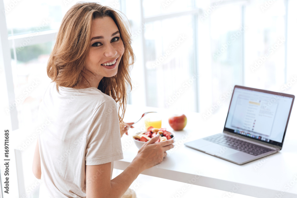 Back view of young woman with breakfast and laptop looking camera Back view of young woman with breakfast and laptop looking camera