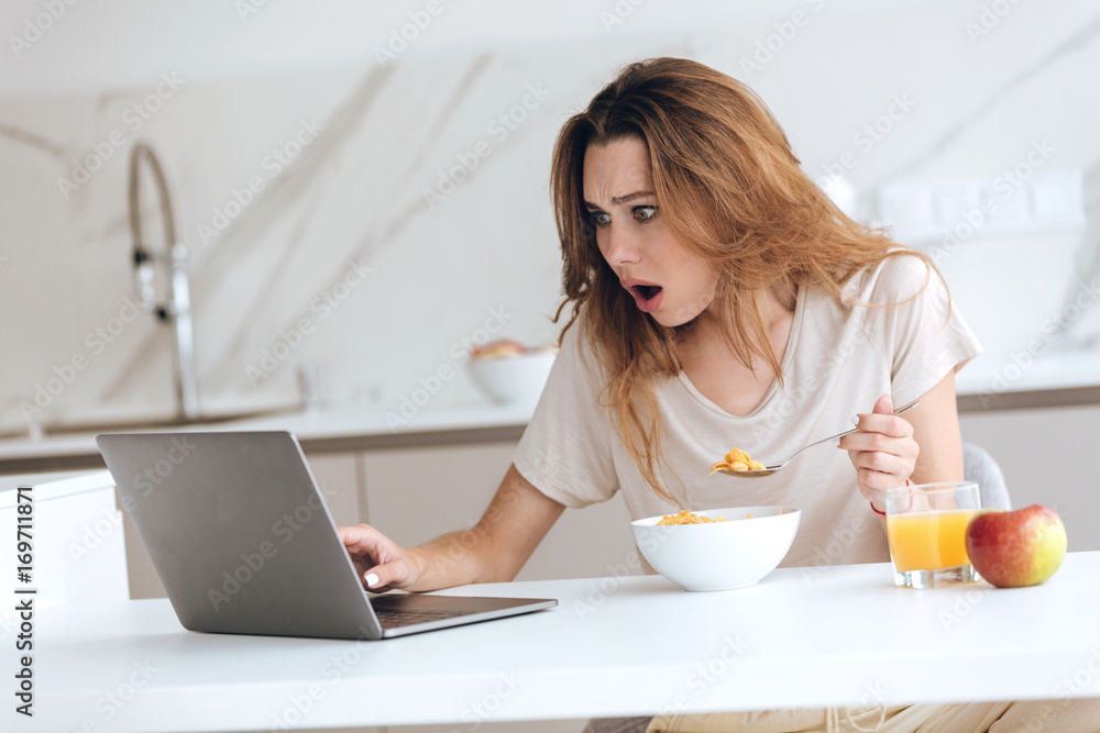 Displeased young woman using laptop in kitchen Displeased young woman using laptop in kitchen