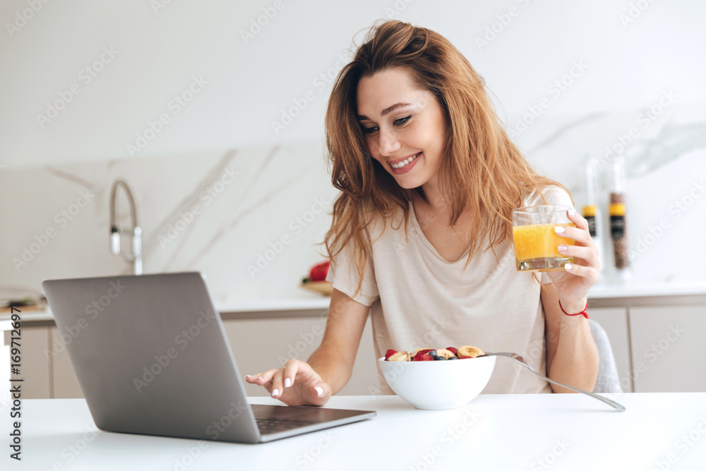 Positive woman with juice using laptop in the kitchen Positive woman with juice using laptop in the kitchen