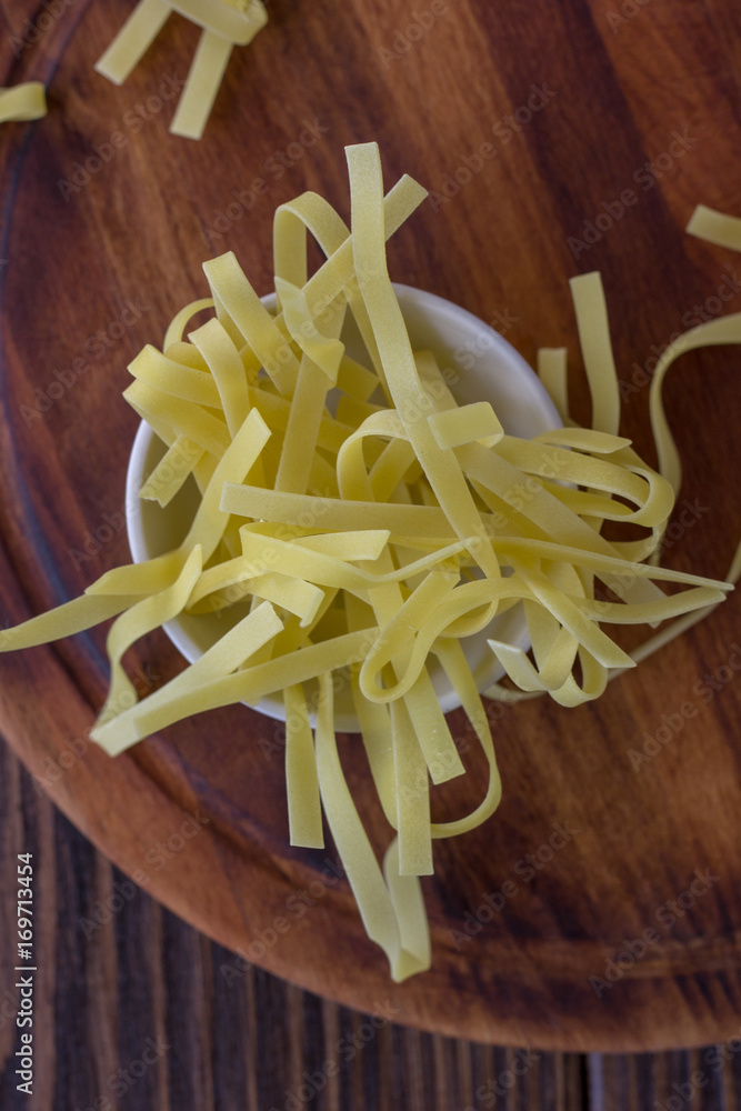 Dry italian pasta on ceramic bowl over wooden background.