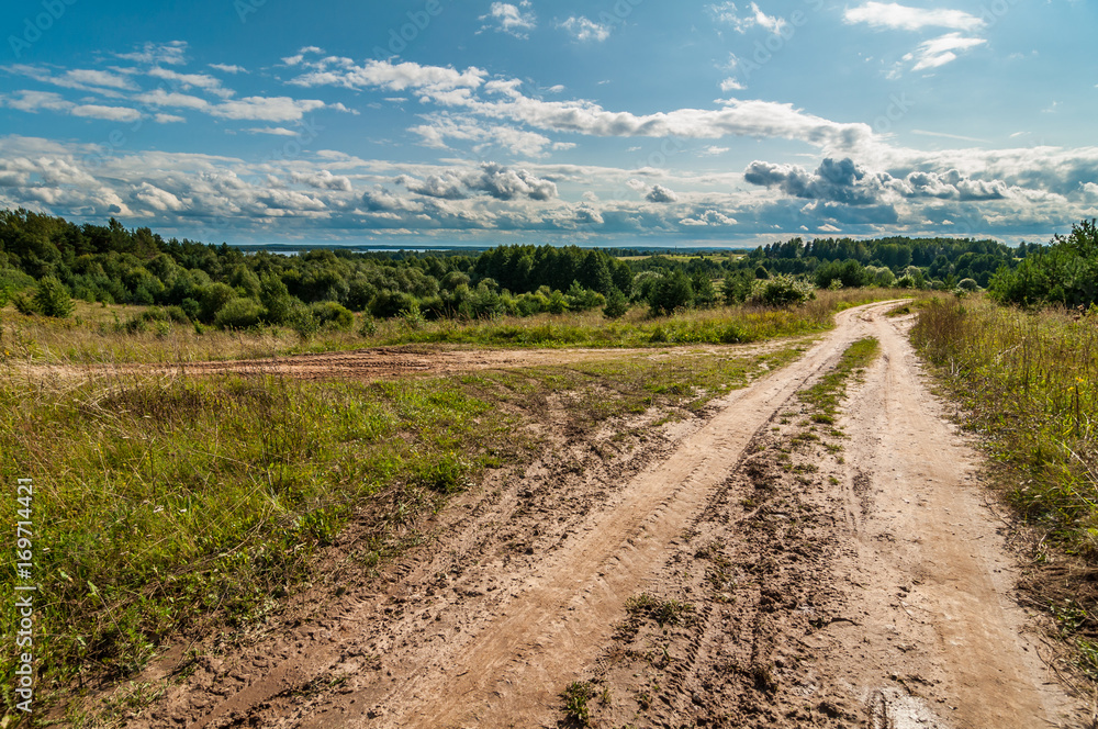 rural dirt road in a hilly area under a blue cloudy sky