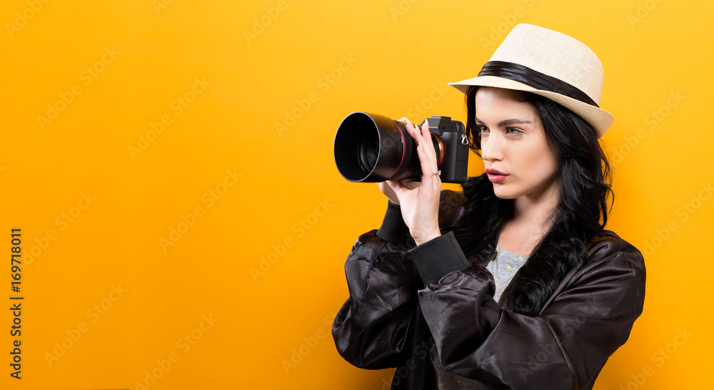 Young woman holding a camera on a yellow background Young woman holding a camera on a yellow background