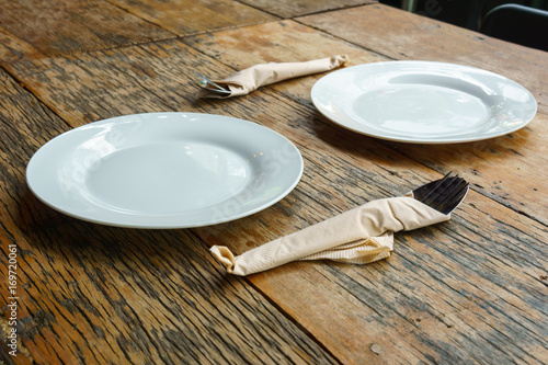 two empty white dishes  with cutlery on the old wooden table. food and tableware concept.