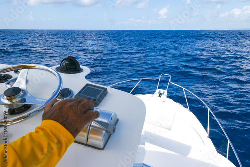 Hand of captain on  the speed switch and steering wheel of fishing motor boat in the blue ocean during fishery day