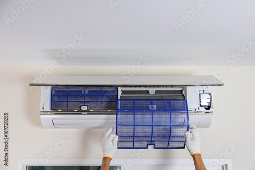 Man's hand is wearing a glove removing the air filter of the air conditioner for cleaning.