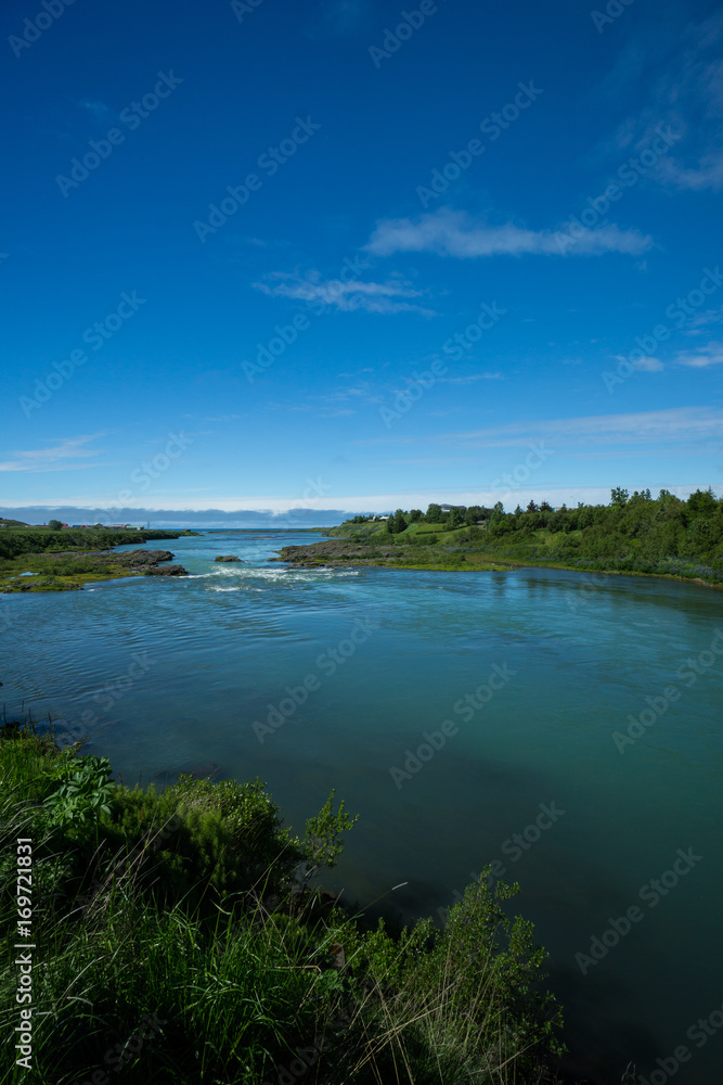 Iceland - Natural blue stream flowing into the ocean between green landscape at blonduos