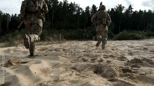 Military soldiers with weapons running on sand back view. Military man