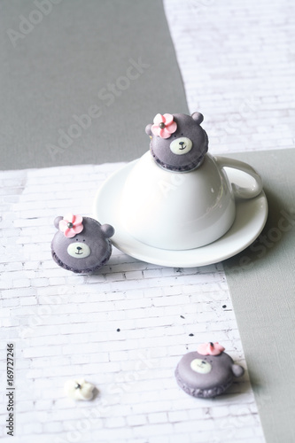 Teddy Bear Macarons with Black Sesame Filling, on white upside down cup, on light grey background. 