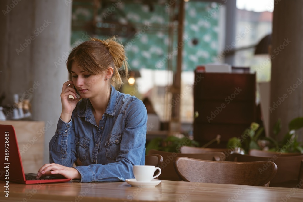 Beautiful woman talking on mobile phone while using laptop Beautiful woman talking on mobile phone while using laptop