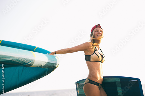Pretty smiling Caucasian woman kitesurfer walking on the beach with her kite