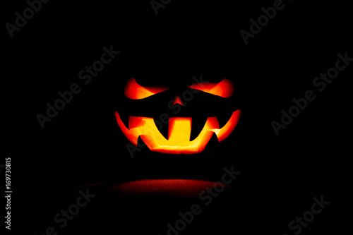 A very terrible Halloween pumpkin, with a terrible look and a smirk of a villain, in the dark