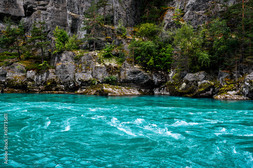 Turquoise water of a river with rocks, cliffs and trees in the background