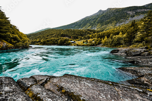 Turquoise water of a river with rocks, cliffs and trees in the background © Julian