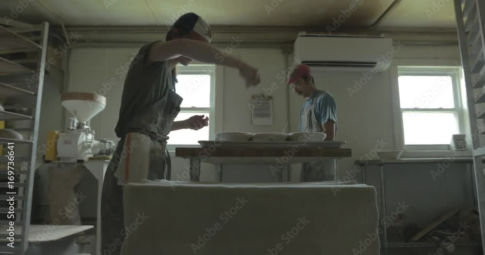 A baker sprinkles wheat flour on bread pans while working with bread dough for baking. A baker sprinkles wheat flour on bread pans while working with bread dough for baking.