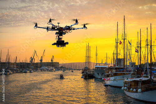 Afternoon sunset between clouds reflected over calm sea water, blue and orange colors. Sailboats with their masts in row at the marina
