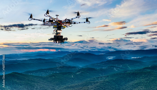 The drone with the professional cinema camera flying over the misty mountains at sunset.