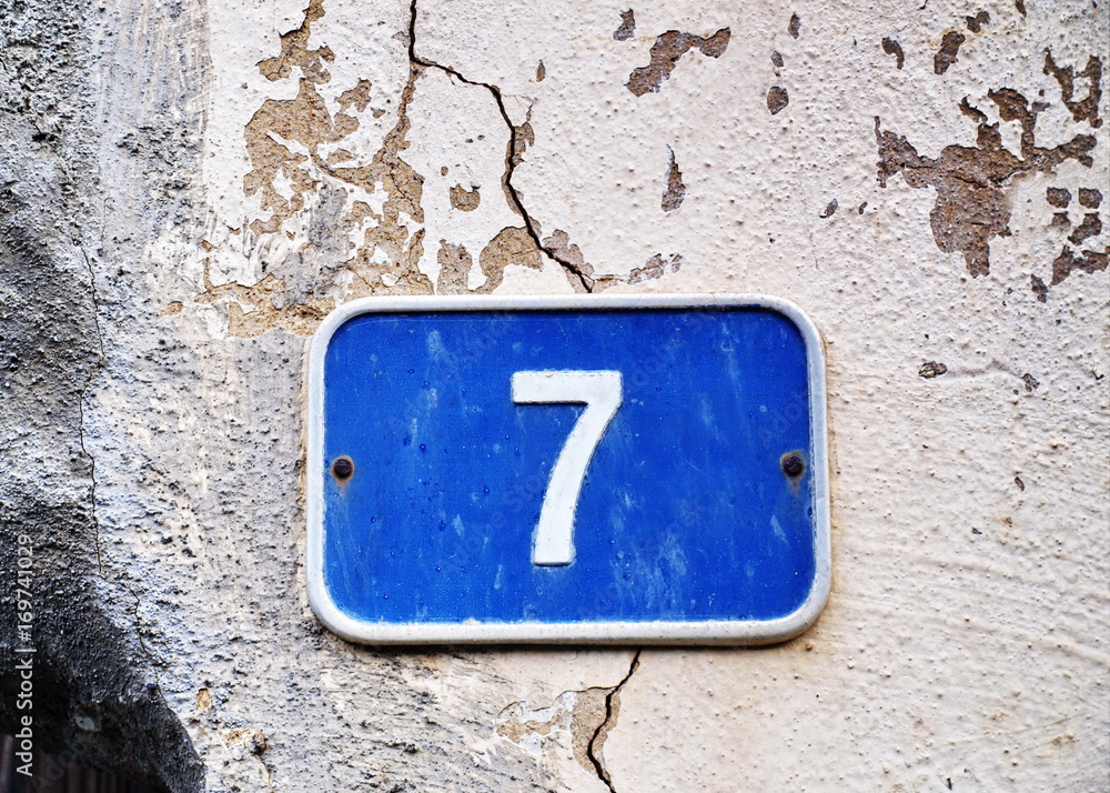 Blue Seven - blaues Schild 7 auf rissiger Wand Blue Seven - blaues Schild 7 auf rissiger Wand