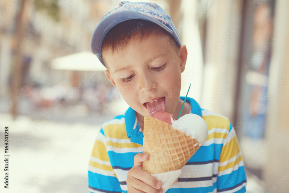 Cute European boy eating ice cream cone in a town street.