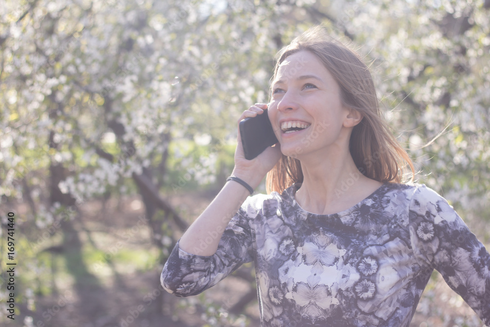 beautiful young womfn in spring park using cellphone and having fun, flower background beautiful young womfn in spring park using cellphone and having fun, flower background