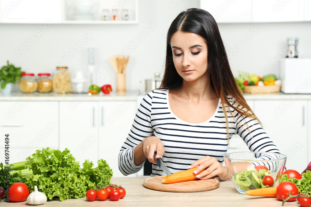 Beautiful young woman cooking salad in the kitchen