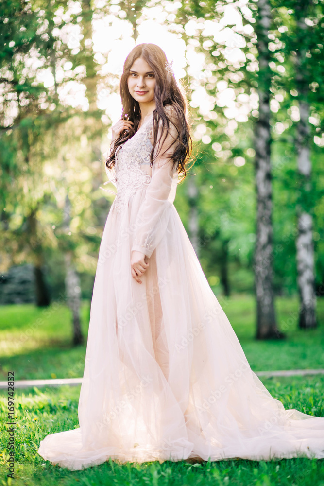 beautiful young girl bride brunette in delicate Bridal boudoir gown of lace and tulle in beige color is outdoors, in a Park with trees, birches beautiful young girl bride brunette in delicate Bridal boudoir gown of lace and tulle in beige color is outdoors, in a Park with trees, birches