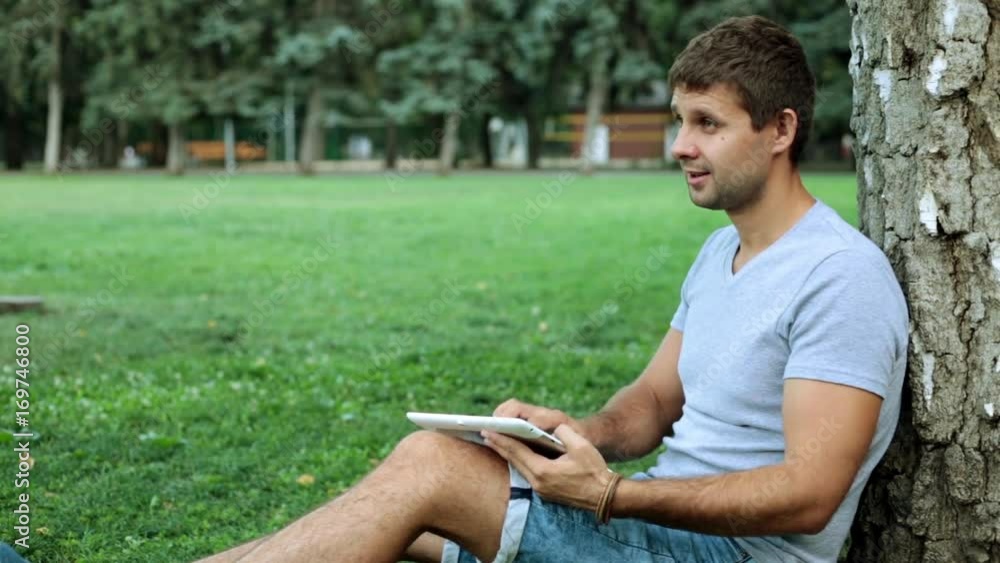 A man is using a tablet computer in the park. A man is using a tablet computer in the park.