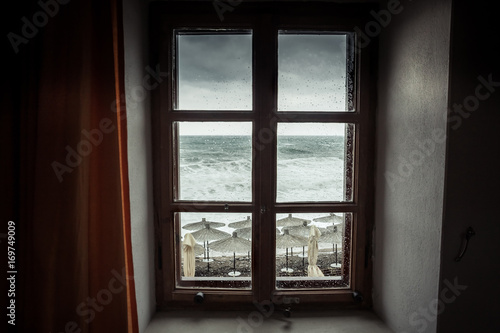Vintage window with dramatic sea view with big stormy waves and dramatic overcast sky during rain and storm weather in fall season on sea coast