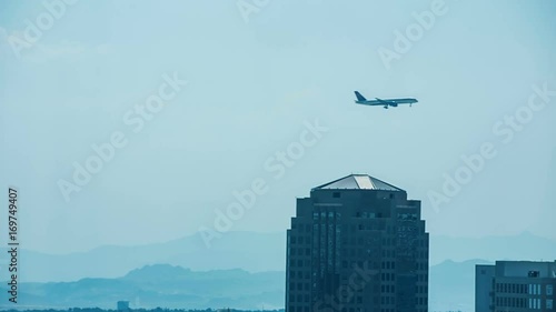 Airplane Flies Over Buildings in Las Vegas. an airplane flies left to right over a few buildings towards airport in Las Vegas with mountains in the background

