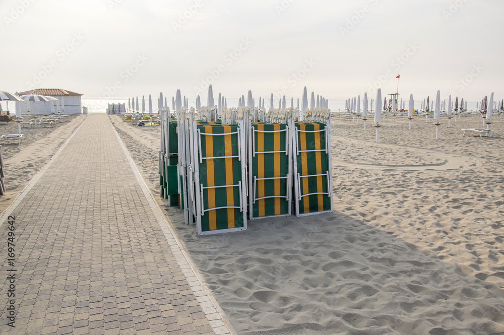 Beach with closed umbrellas and sunbeds, sun loungers and umbrellas, early morning in Sottomarina, Italy, Europe Beach with closed umbrellas and sunbeds, sun loungers and umbrellas, early morning in Sottomarina, Italy, Europe