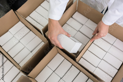 High-angle close-up view of the hands of a manufacturing worker putting packed products, in cardboard boxes before export or shipping during manual work in a cosmetics factory photo