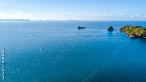 Fototapeta Naklejka Na Ścianę i Meble -  Aerial view on a yacht racing along tiny island ocean on sunny day. Coromandel Peninsula, New Zealand
