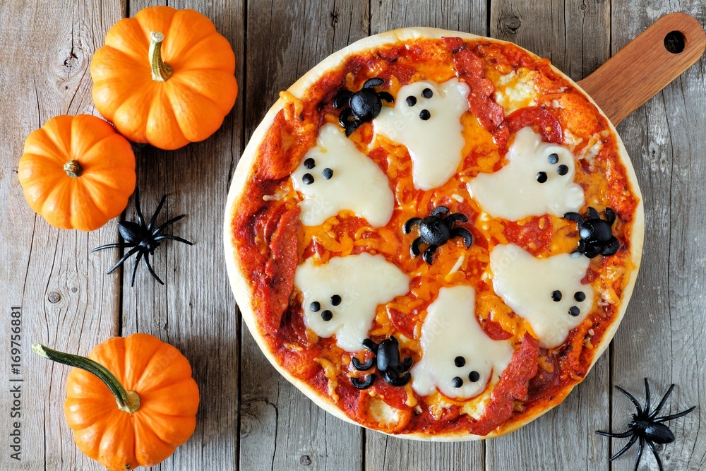 Fototapeta premium Halloween pizza with ghosts and spiders, above scene with decor on a rustic wood background