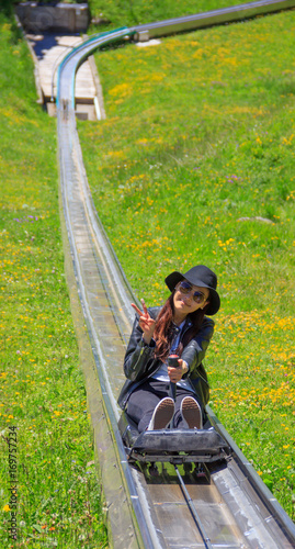Obraz na plátně Asian woman riding summer toboggan (sled) down a hill through the beautiful flower meadow in Oeschinensee, Kandersteg, Switzerland